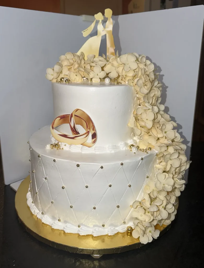 Two-tier white wedding cake with gold rings and cream flowers